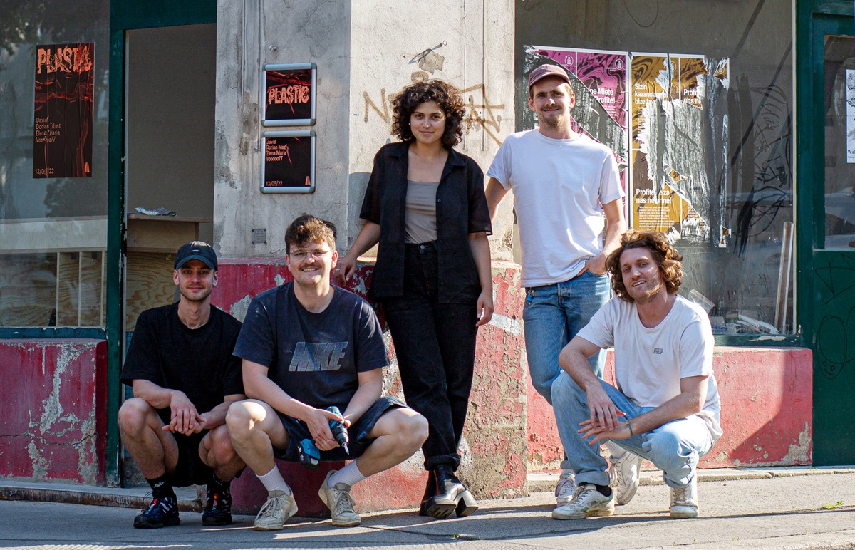 Fünf Persoenen stehen vor einem Eckhaus. Von rechts scheint die Sonne, die linke Haushälfte liegt im Schatten. Das Haus hat eine grau und rote Fassade. Das Team von Plastic Dreams präsentiert sich vor dem Shop.