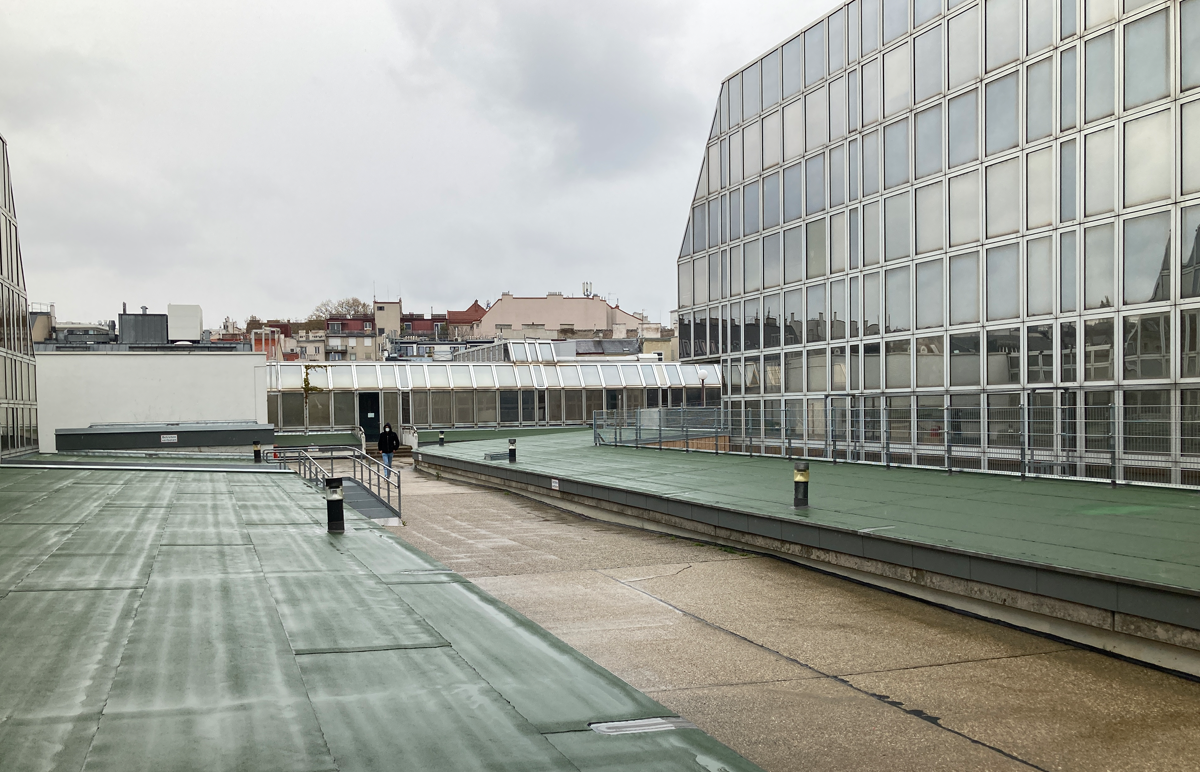 Dach des Gebäudes im Regen mit Wiens Dächern im Hintergrund.