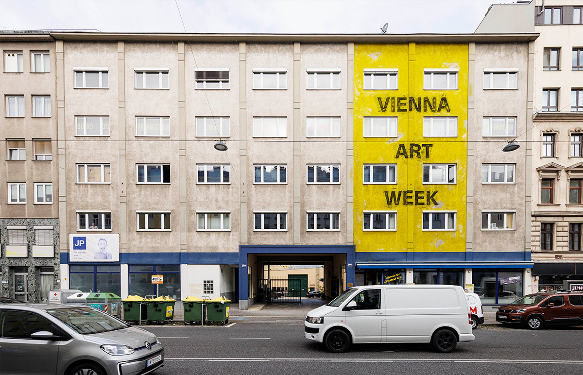 Die Fassade eines vierstöckigen Bürohauses von der Straße aus, ein Teil ist mit gelber Farbe betrichen.