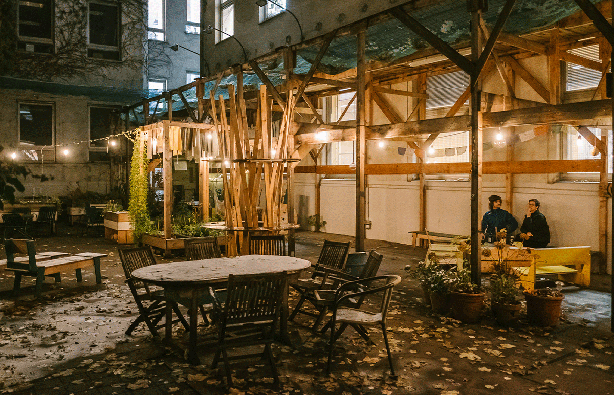 abendliche Stimmung im Innenhof des Creative Clusters. Mittig ein Tisch mit Stühlen und ein beleuchtetes Holzgerüst