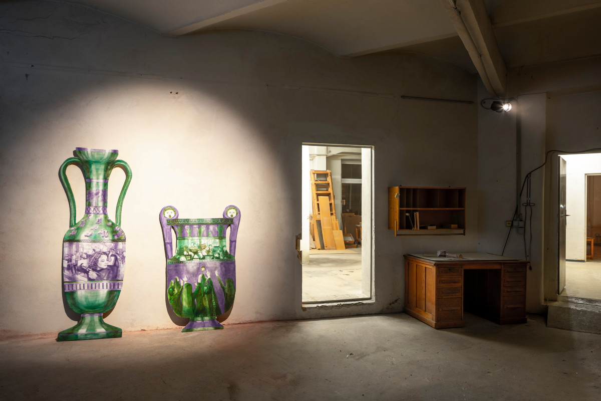 Eine beleuchtete Wand neben einer Tür, eine überdimensionierte Vase als Skulptur vor der Wand.
