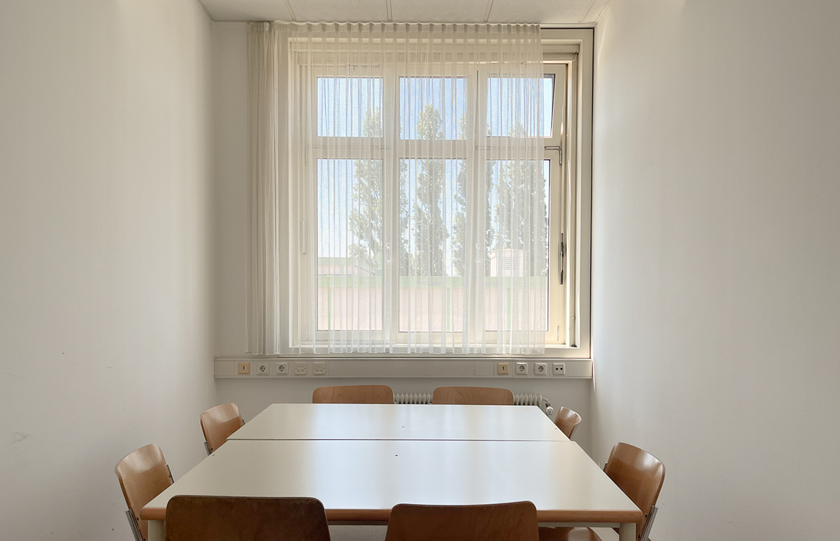 Blick in einen der kleineren Räume mit zwei aneinandergestellten Tischen und acht Stühlen.