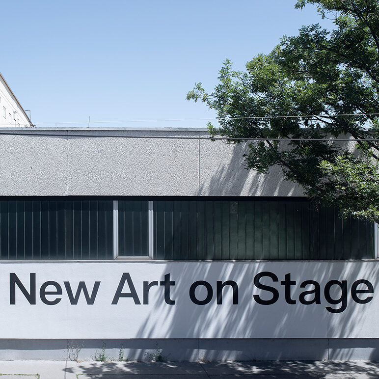 new art on stage steht mit großen Lettern mit einem schwarzen pfeil auf einer häuserfront von einem grauen bürotrakt.